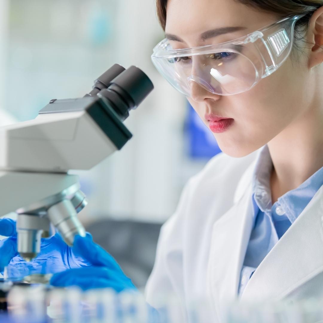 japanese life science expert wearing protective goggles looking at microscope