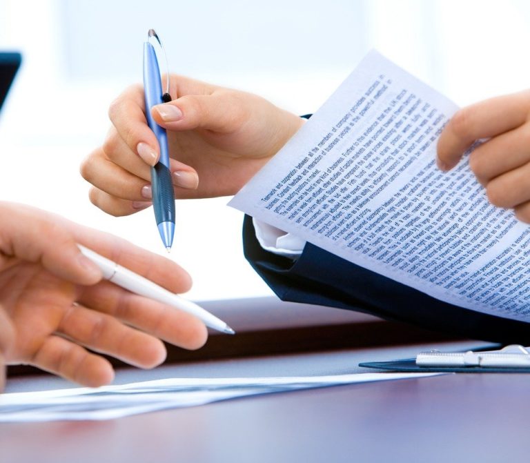 hands of two people with papers and one hand holding a pen