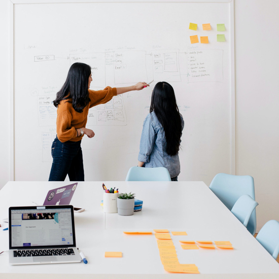 two women discussing business process on whiteboard