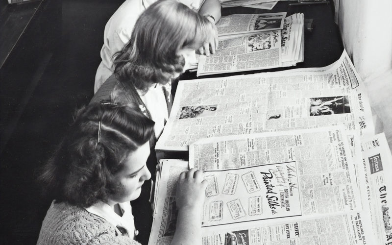 black and white photograph of women reading advertisements in newspapers.