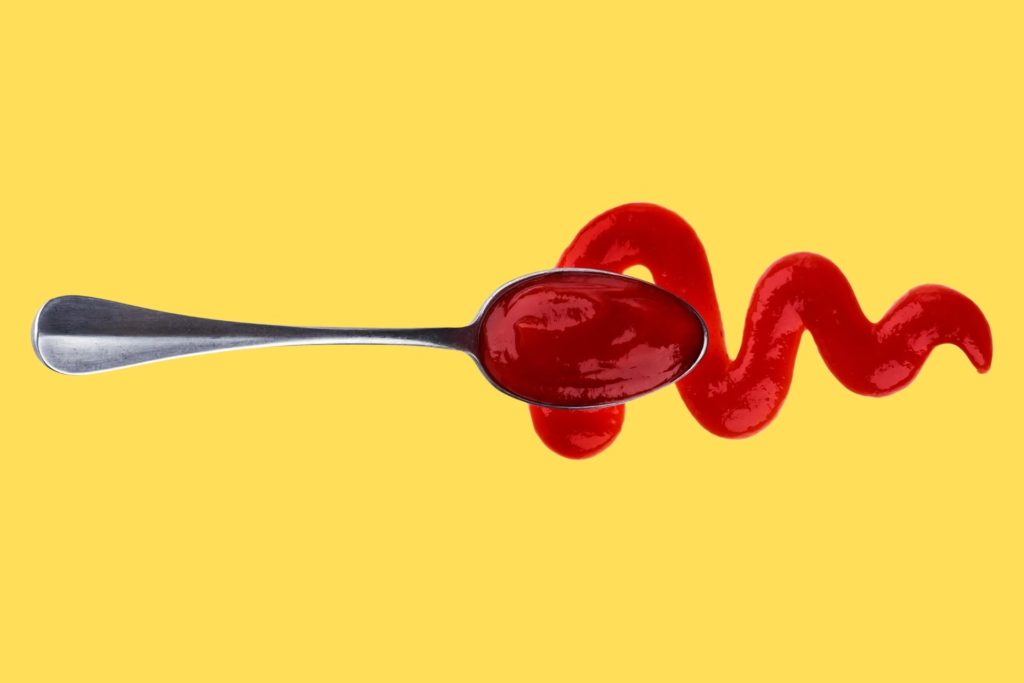 ketchup dripping from spoon against yellow background