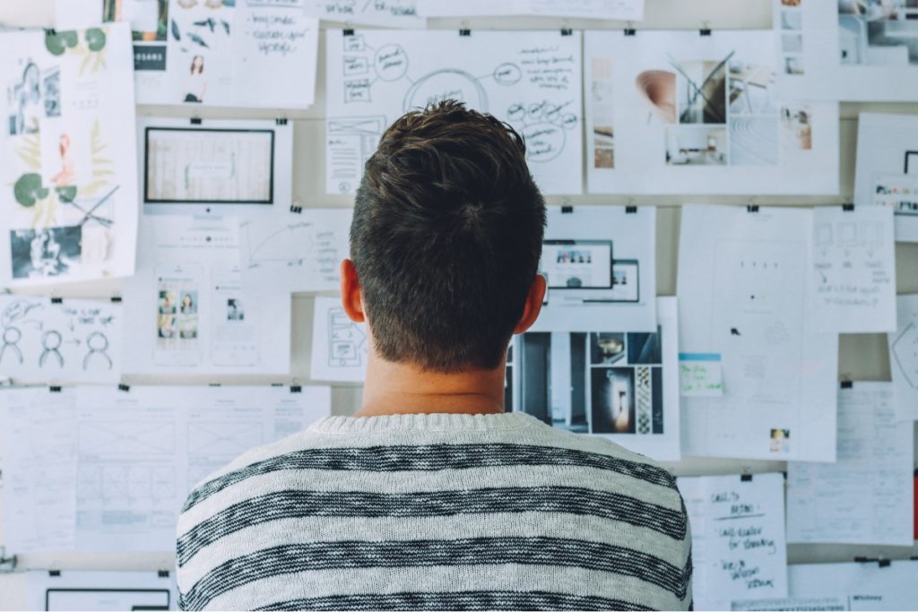 Man wearing black and white stripe shirt looking at many printer papers on the wall. Symbolizes the wide scope of linguistic testing