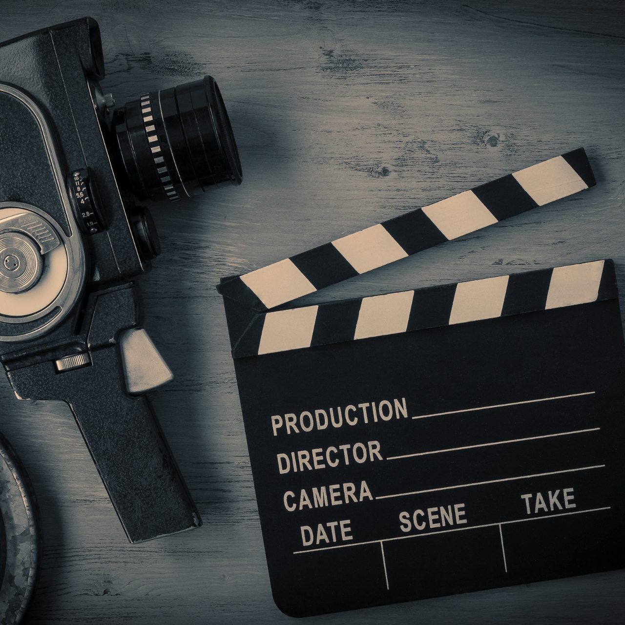 Old movie camera, movie reels and a clapperboard lying on a wooden board. View from above