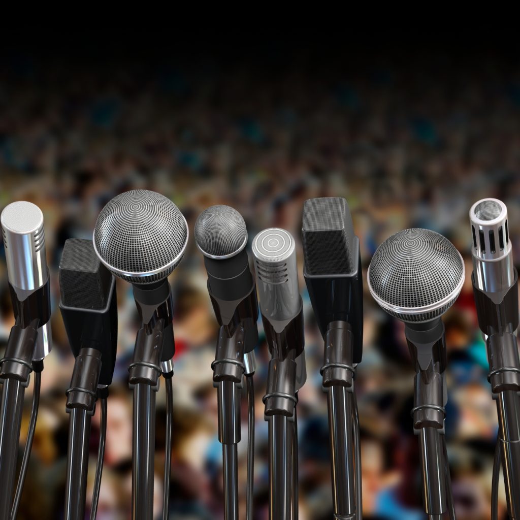 many microphones stacked with a wide audience blurred in background